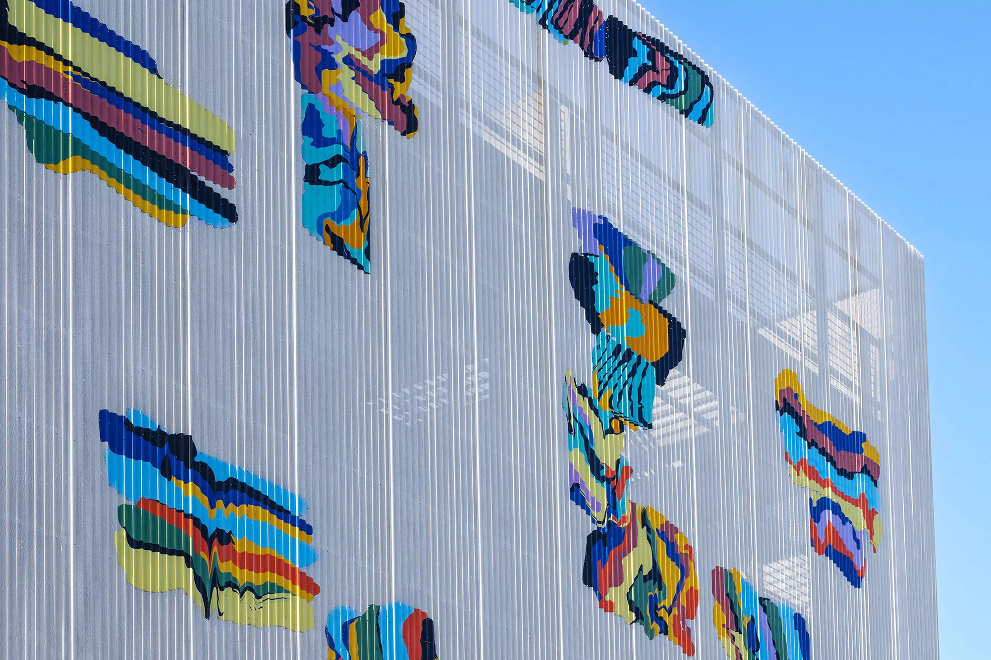 Exterior of a modern building featuring a white slatted facade with colorful abstract designs against a clear blue sky.