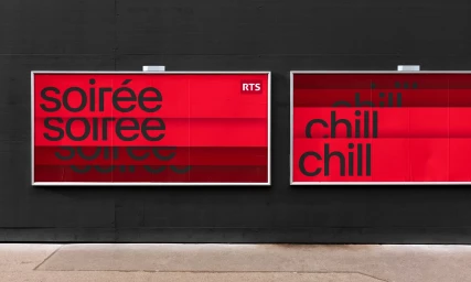 Two rectangular billboard displays with red posters featuring bold black typography mounted on a dark wall.