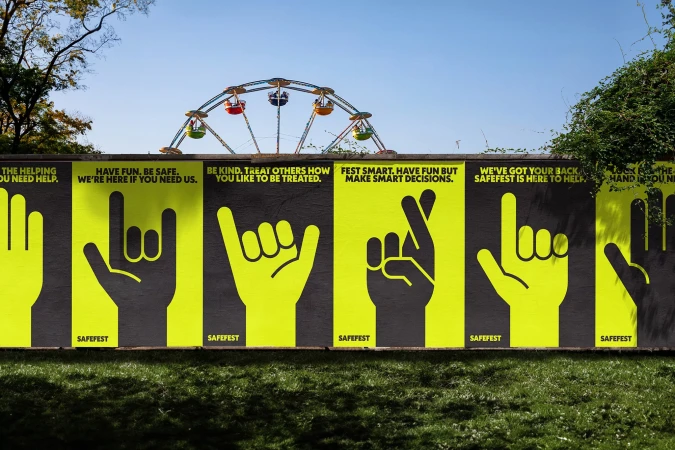 SafeFest wall mural with hand graphics and safety messages, viewed outdoors with green lawn and a colorful ferris wheel in the distance.