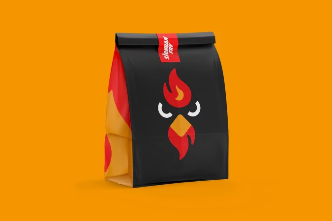 A black paper bag with a stylized fiery chicken logo sits against a bright orange background, simple studio product shot.