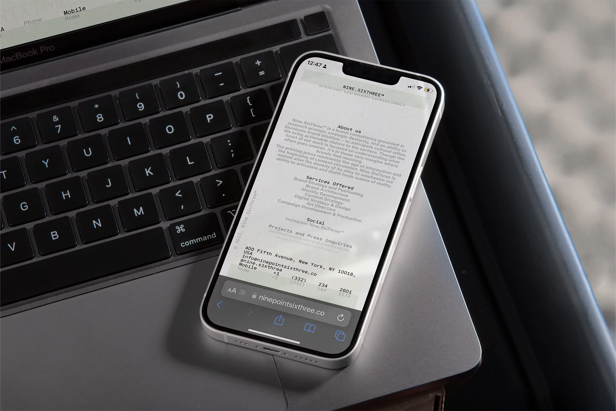 Silver iPhone displays a website next to a Macbook Pro keyboard, showcasing digital interface and technology on a clean gray surface.