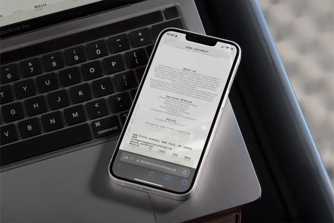 Silver iPhone displays a website next to a Macbook Pro keyboard, showcasing digital interface and technology on a clean gray surface.