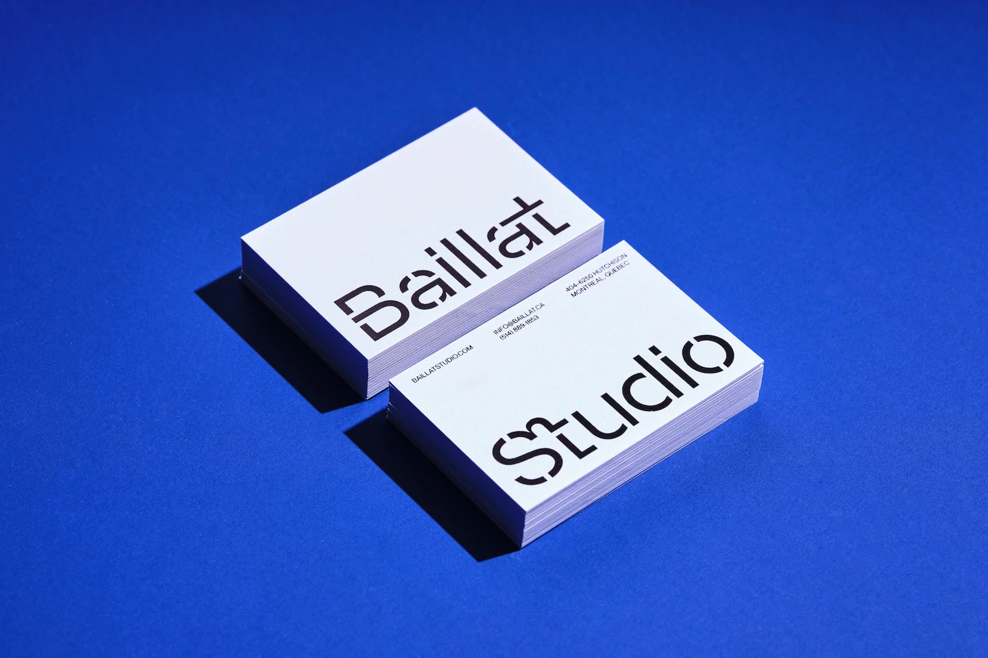 Stack of white business cards with modern stencil type on a blue background in a studio, showcasing Baillat Studio branding.