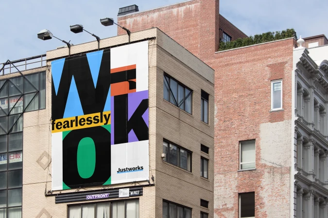 Large, colorful 'WORK fearlessly' billboard on a brick building in an urban setting. The Justworks logo is visible at the bottom.