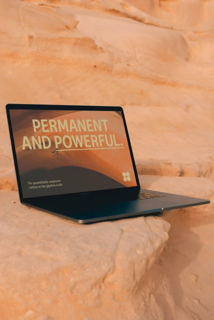 A laptop rests on a sandstone rock formation outdoors displaying text about sustainability on screen in a digitally enhanced shot.