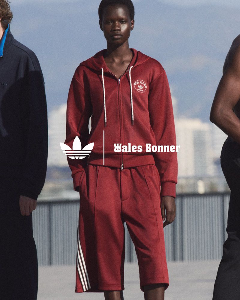 Two adult models showcase Adidas x Wales Bonner maroon tracksuit with stripes, set against a blurred urban backdrop with natural lighting.