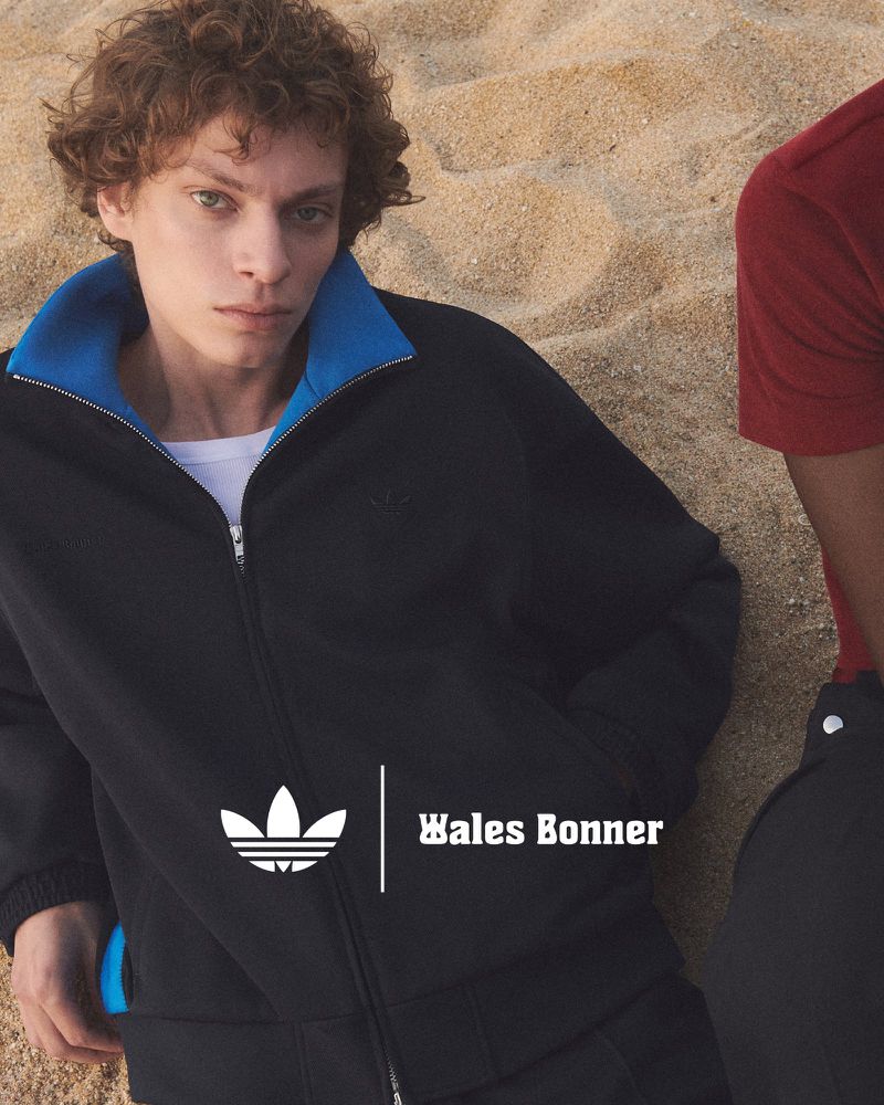 Two fashion models pose outdoors on a beach, wearing Adidas x Wales Bonner tracksuits. One model is lying on the sand.