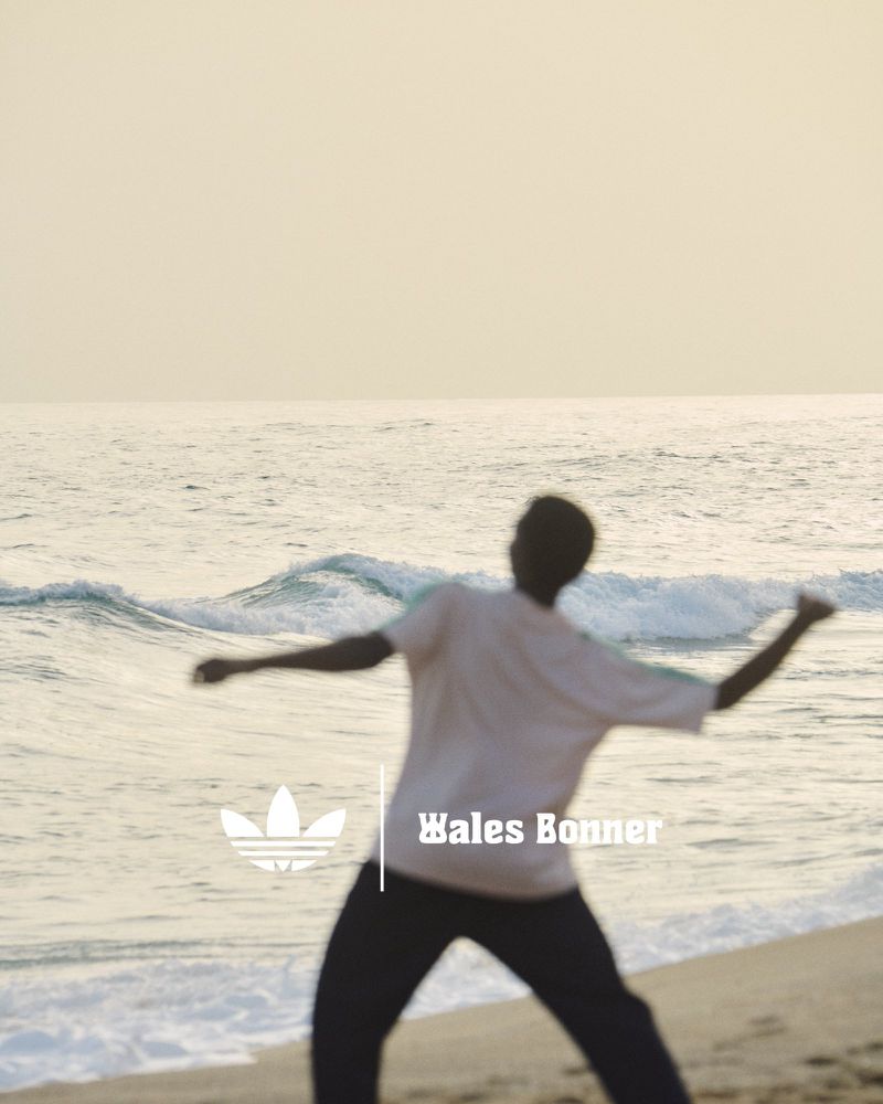An athletic, dark-skinned man wearing sportswear throws an object with force on a beach with ocean waves under an overcast sky.