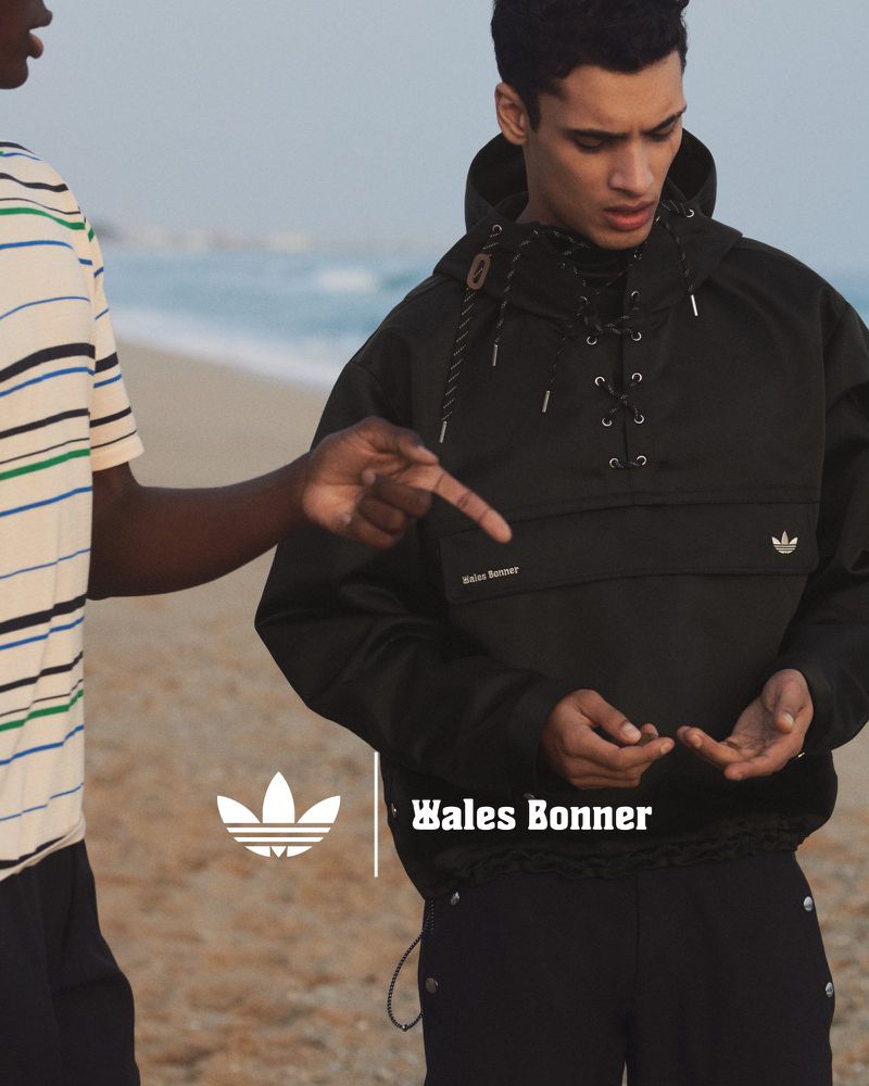 Two men on a sandy beach with the man on the right wearing a dark hooded Wales Bonner x Adidas jacket and dark pants.