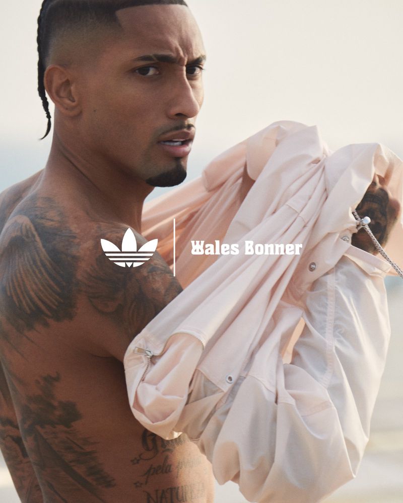 Adult male model in athletic wear poses holding jacket, with the Adidas logo and 'Wales Bonner' text visible against a light backdrop.