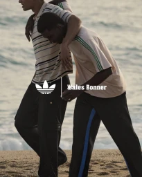 Two men walking together along a sandy beach wearing striped polo shirts and athletic trousers in an Adidas Originals by Wales Bonner campaign