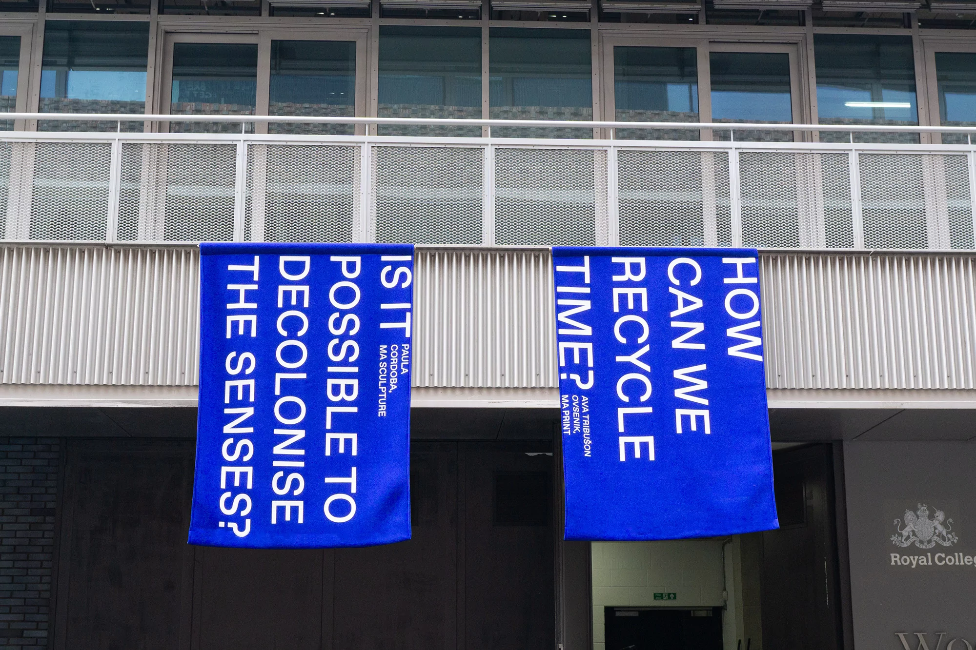 Two blue banners with white text hang on the side of a building, promoting 'MA Sculpture' and 'MA Print' art installations.