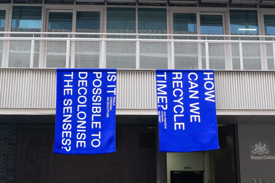 Two blue banners with white text hang on the side of a building, promoting 'MA Sculpture' and 'MA Print' art installations.