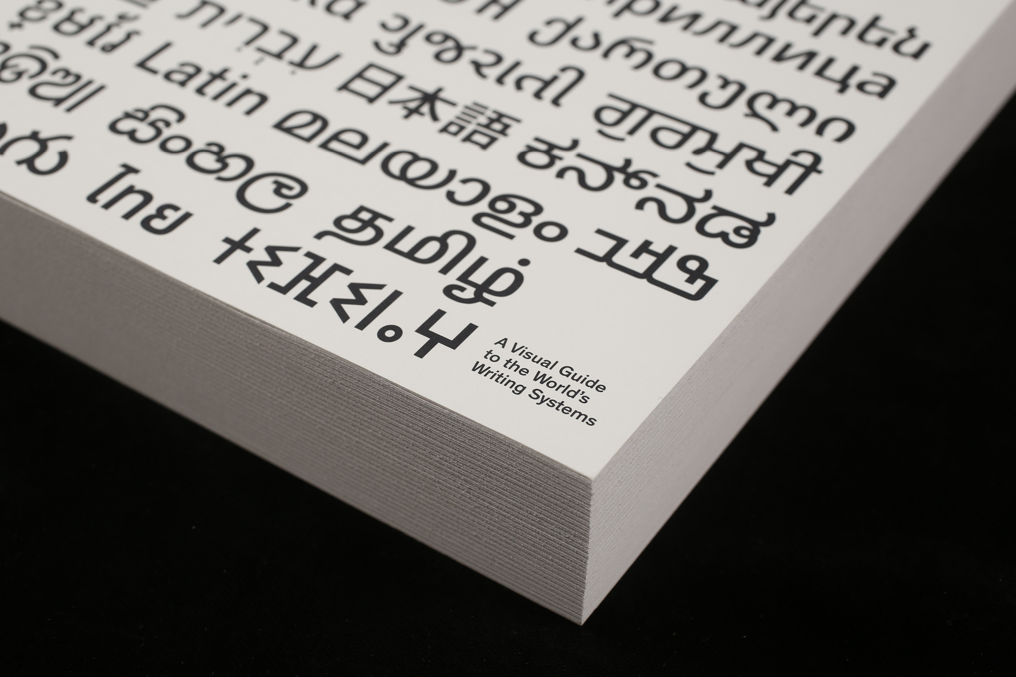 Close-up of a book titled, "A Visual Guide to the World's Writing Systems", featuring multilingual scripts and black text on white pages.