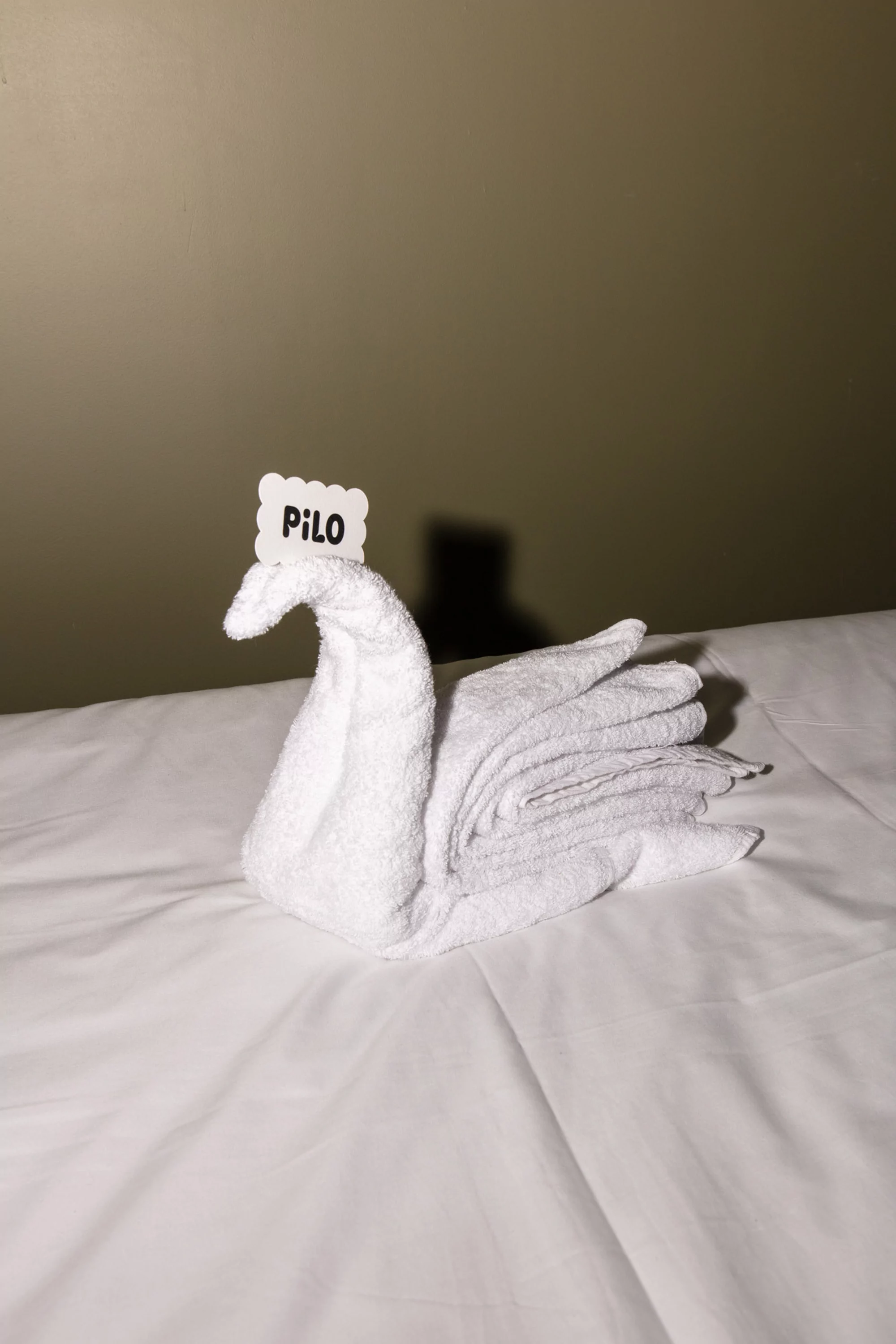 A white swan made from folded towels on a bed with a decorative name tag, conveying a welcoming and elegant hotel experience.