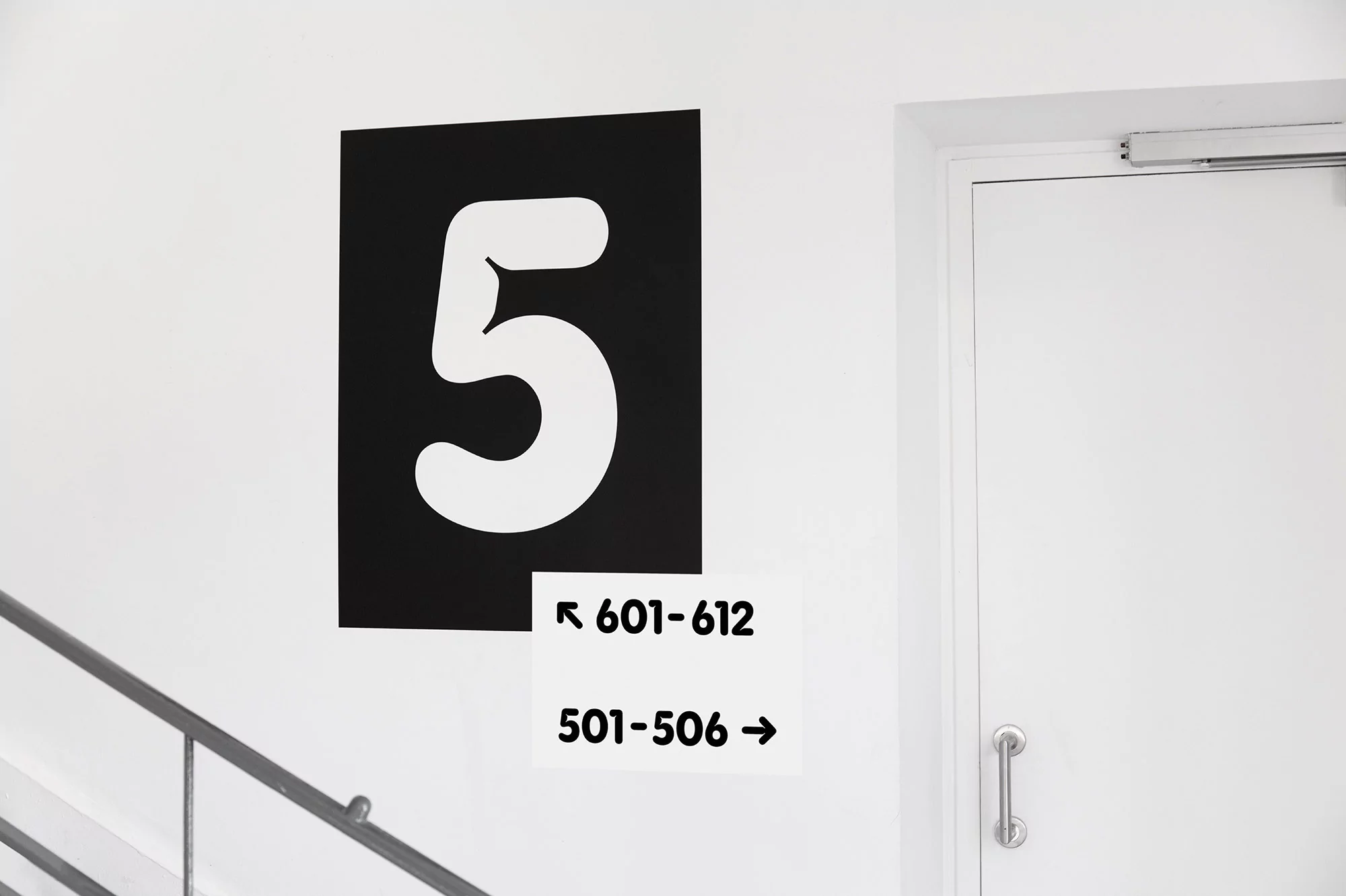 A clear and graphic image showing a large white number 5 on a black square with directional signage next to a white door indoors.