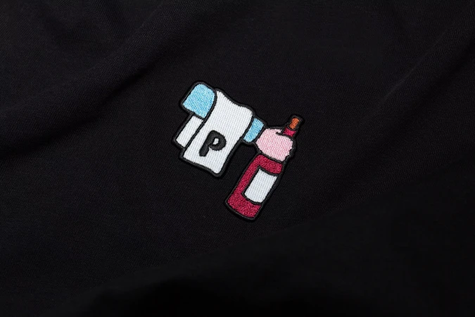 Embroidered patch of a 'P' logo next to a pink and red wine bottle on a black garment, showcasing detail and design.