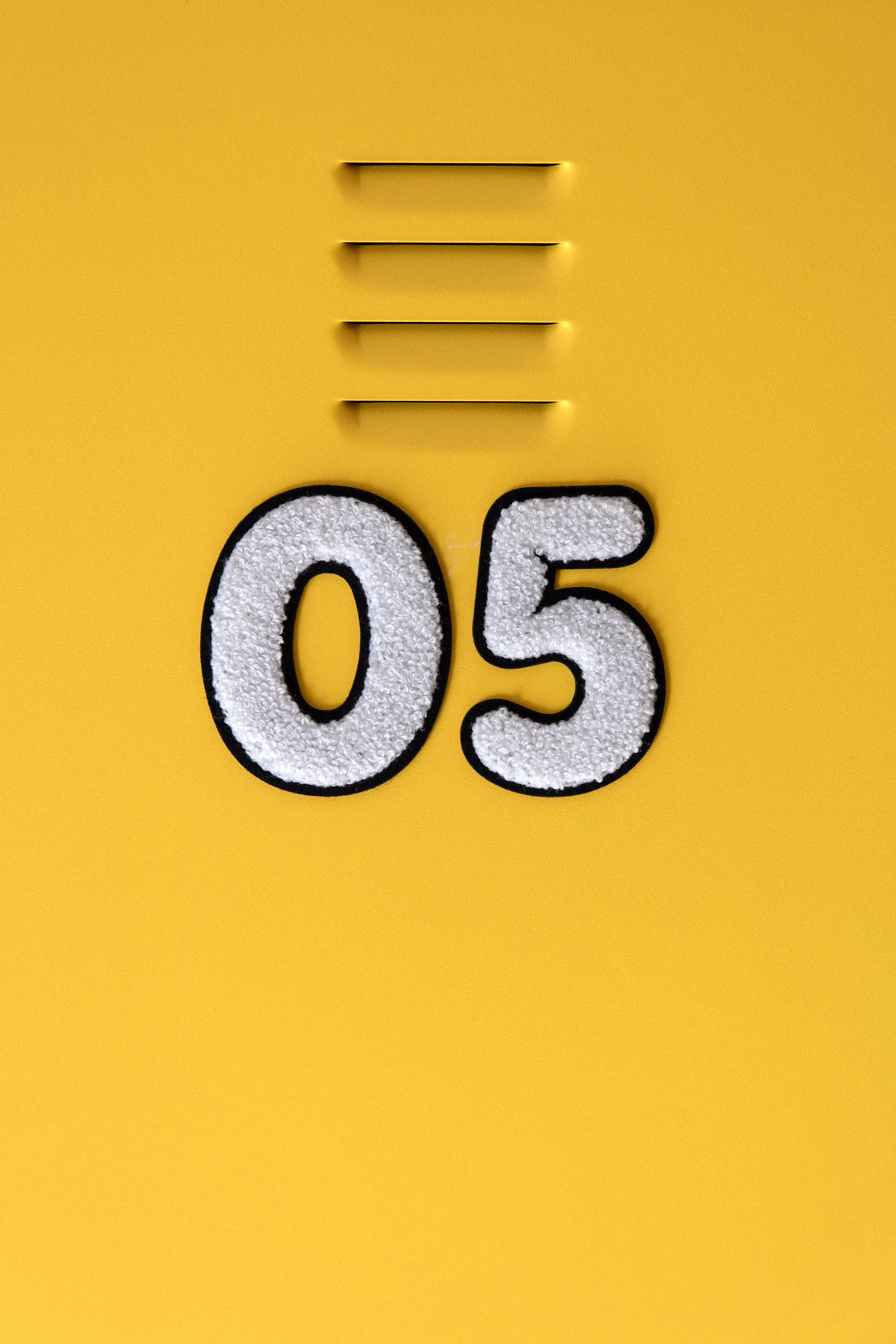 Close-up shot of the number 05 affixed to a bright yellow surface with three horizontal ventilation slots above the number.