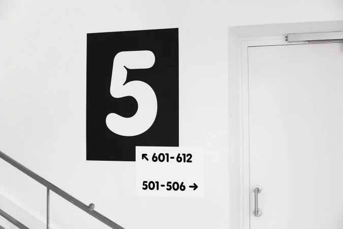 Monochrome architectural signage with a large white number five on a black rectangle next to directional wayfinding labels.