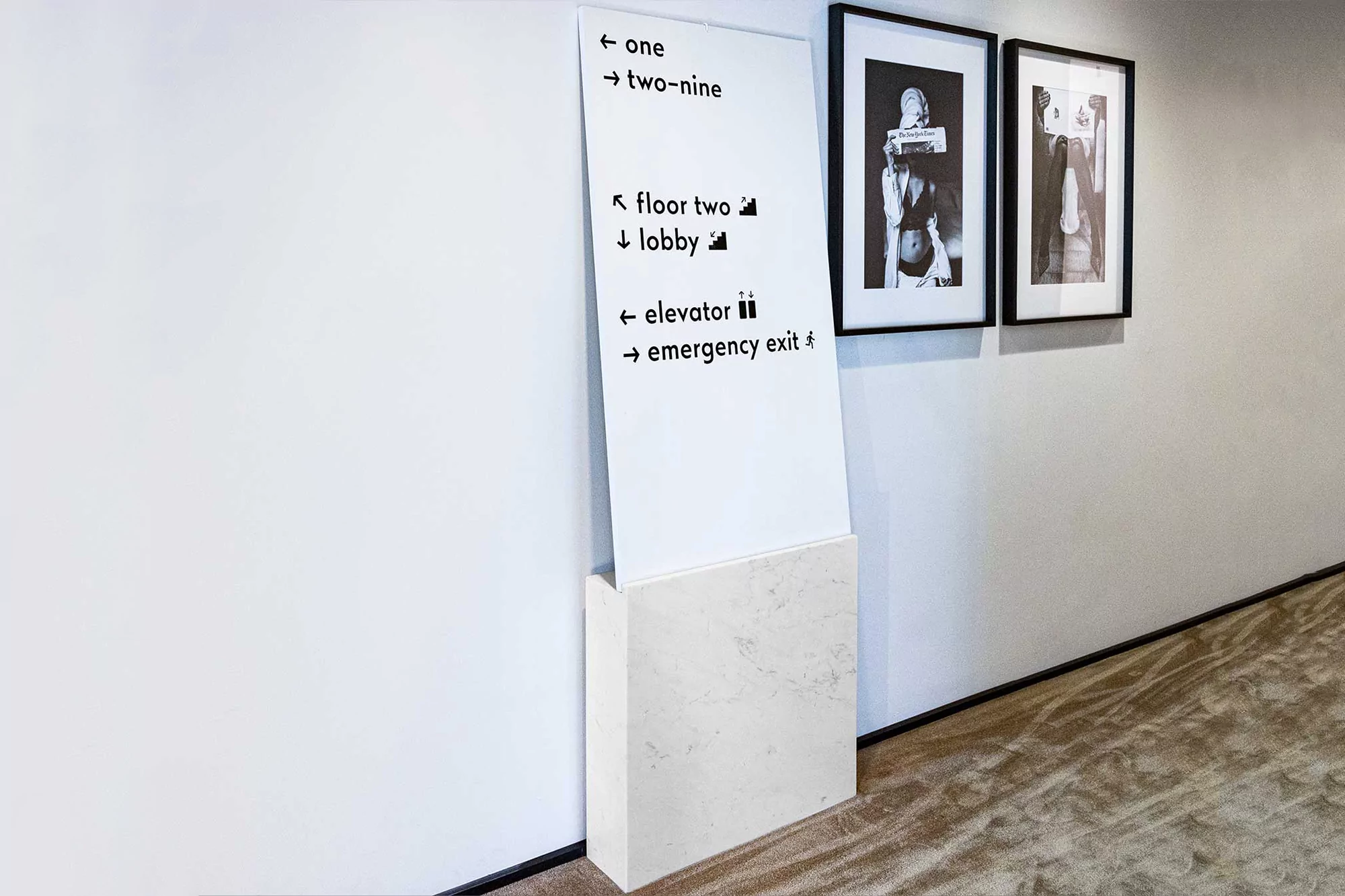 Interior shot of a marble-based sign with wayfinding text, accompanied by two framed black-and-white artworks hanging on a white wall.
