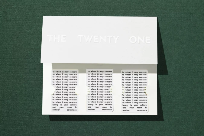 Close-up of a white card with embossed text and printed labels, showcasing a minimalist aesthetic on a green surface.