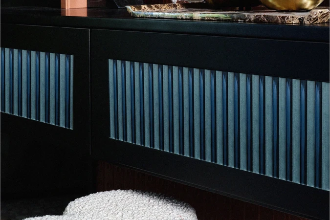 Interior design detail featuring a dark blue cabinet with fluted glass panels and a textured white stool.