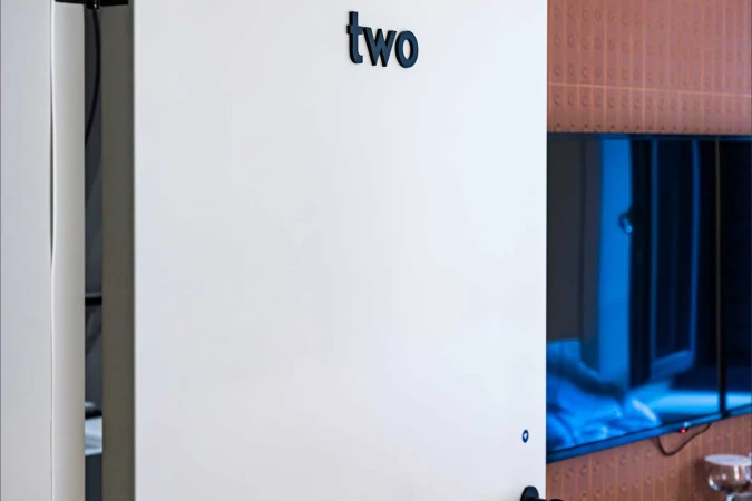 White wall with dark-blue 'two' lettering above a door, next to a television in an interior setting. Minimalist modern design.