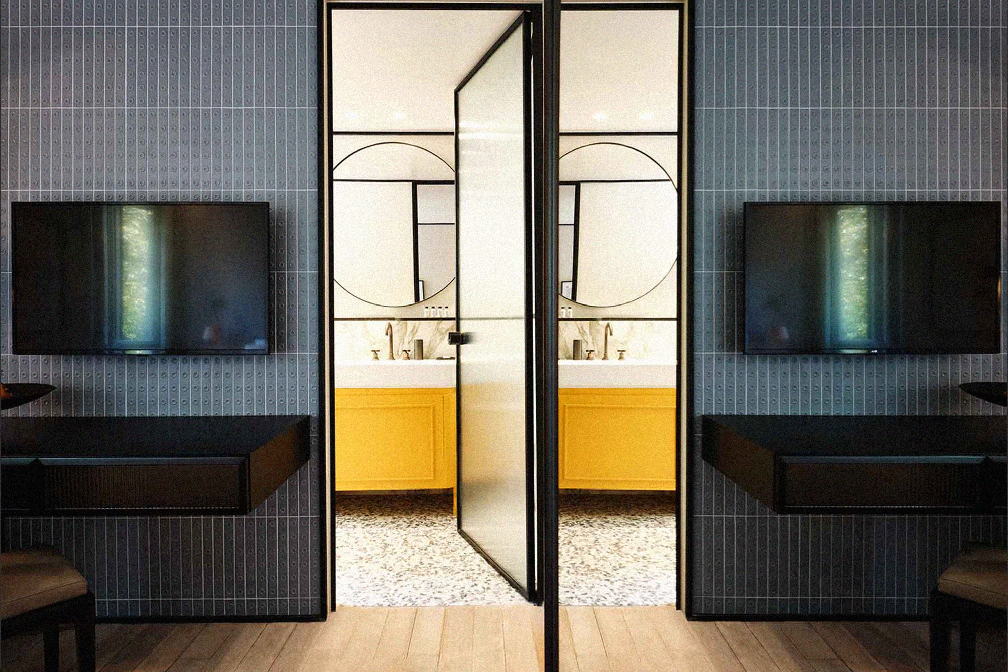 Modern interior featuring a tiled wall, a vanity with a yellow cabinet, and a glass and black frame door, creating a sleek design.