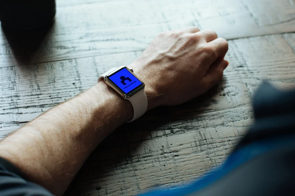 Close-up of a smart watch on a person's wrist showing a display with a silhouette icon, against a rustic wood surface.
