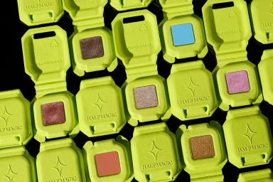 Top-down view of vibrant lime green compostable makeup compacts with Half Magic branding arranged on a dark background