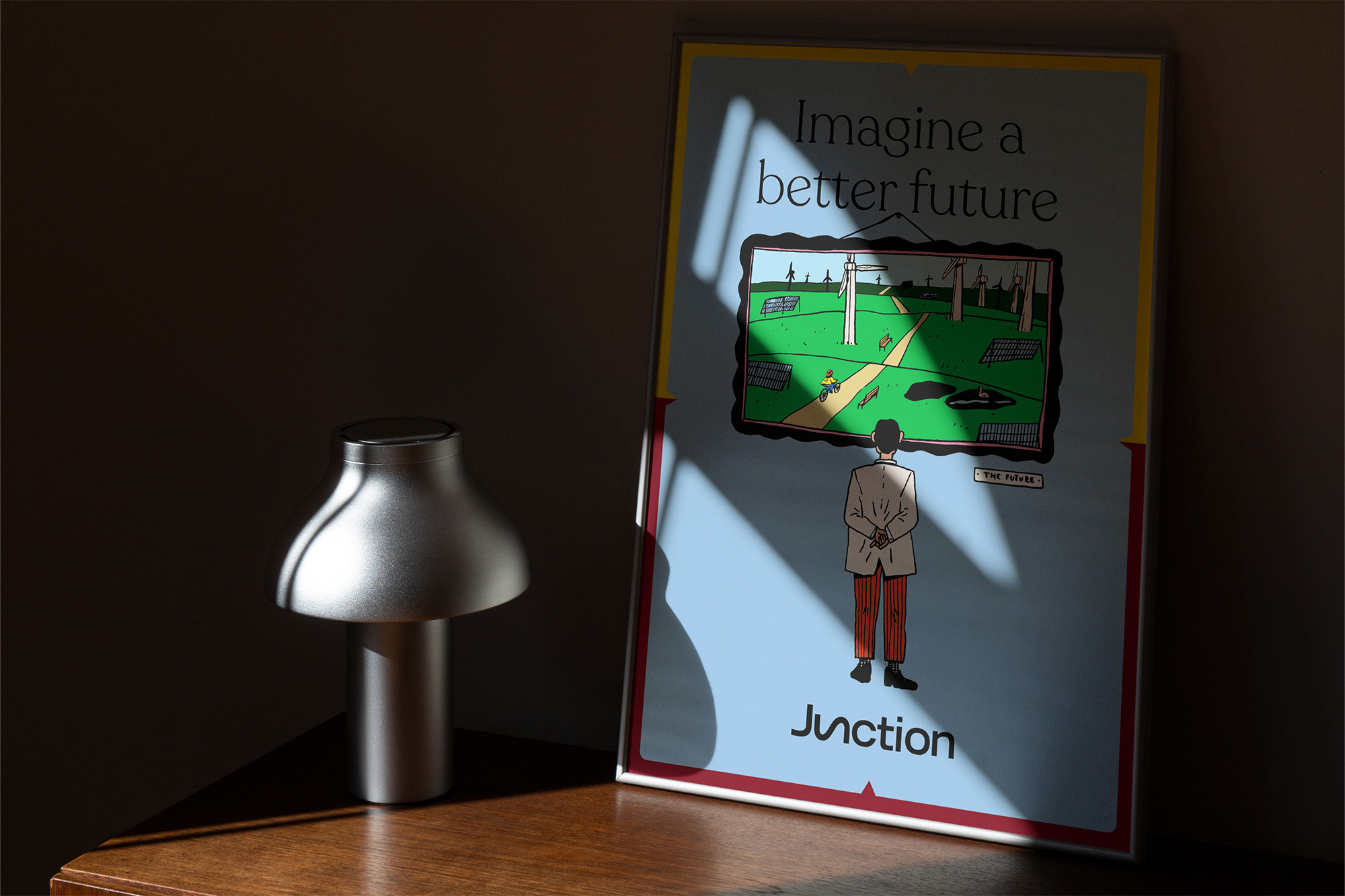 A digitally-created image showcases a poster with an illustration of a man looking towards a wind turbine scene, next to a mushroom lamp on a wooden table.