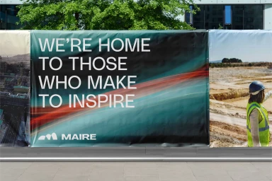 Large outdoor banner for Maire Group featuring white text reading we are home to those who make to inspire against a dark gradient background