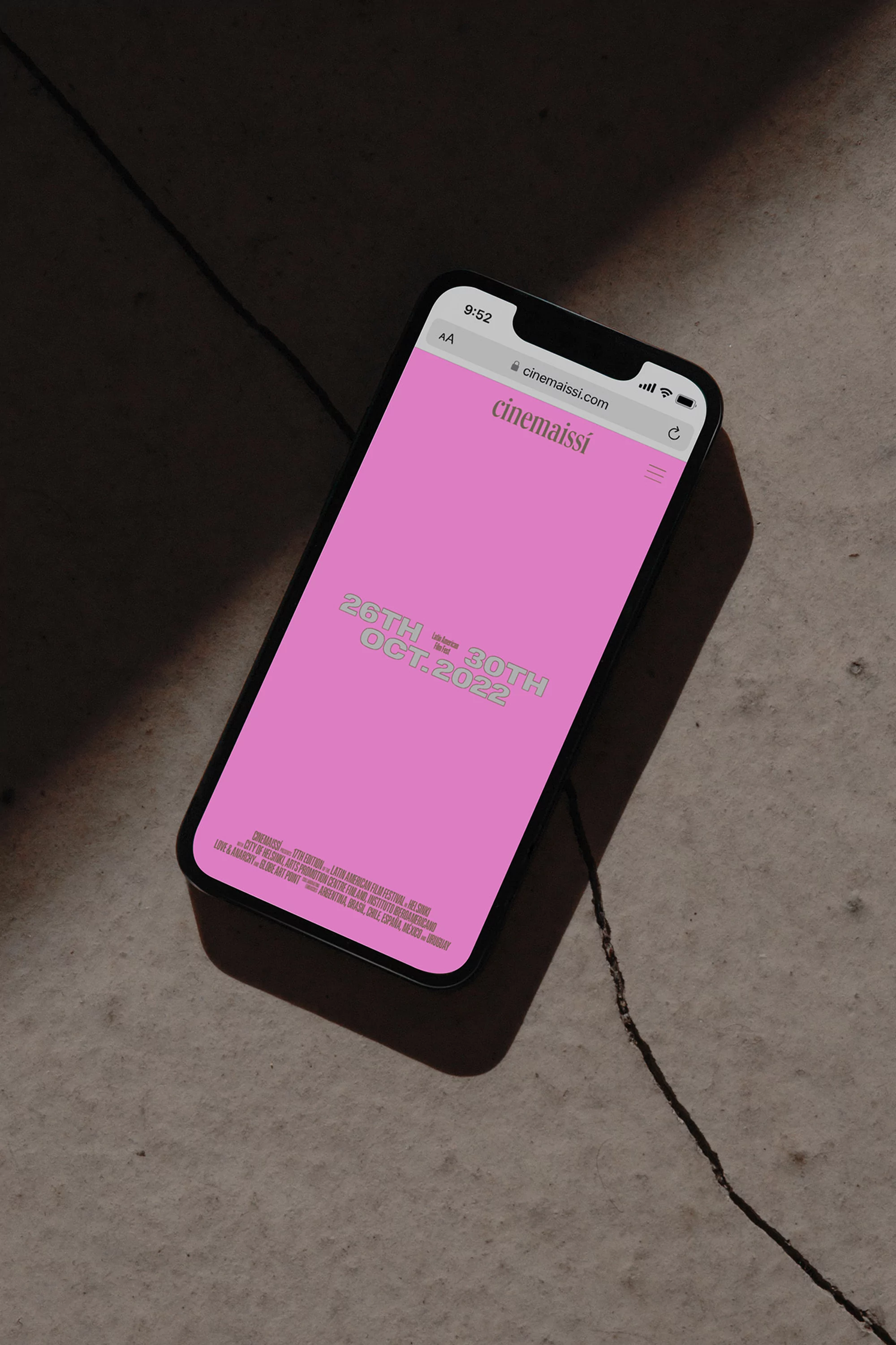 Smartphone displays cinemaissi.org site with a pink screen and event dates against a textured grey background with dark shadows and cord.