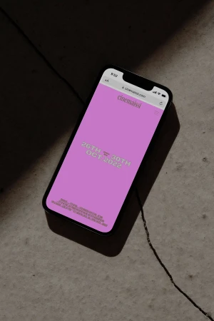 Smartphone displaying a pink mobile website screen with text resting on a dark concrete surface.