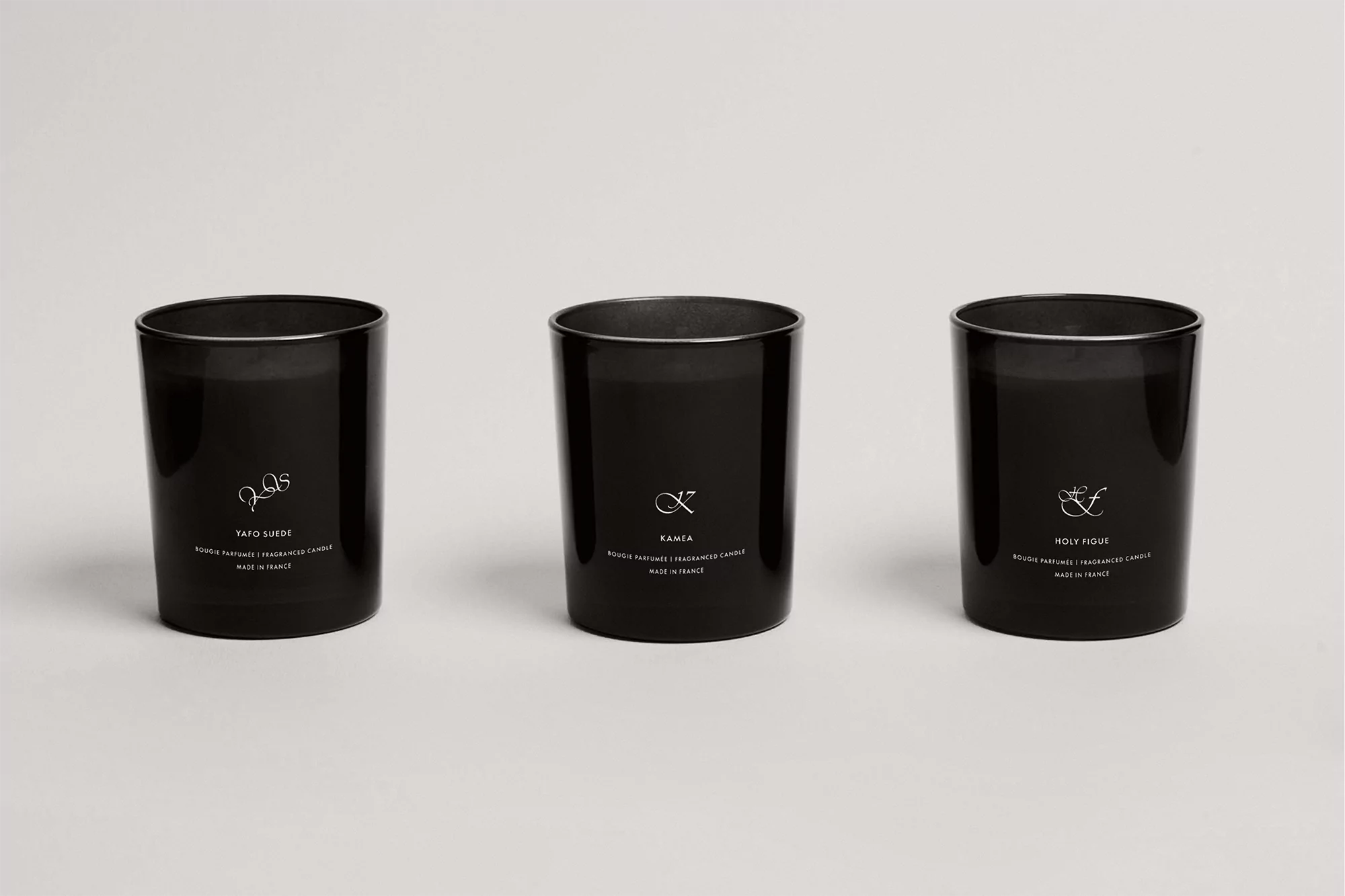 Three black scented candles in clear glass containers on a white surface, displaying minimalist labels with delicate typography and symbols.