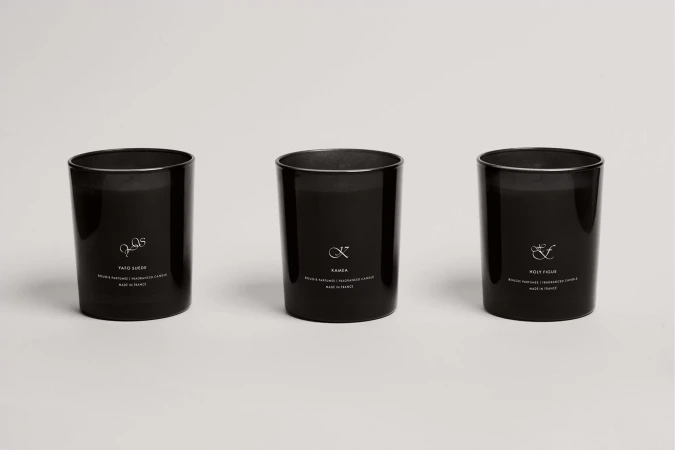 Three black scented candles in clear glass containers on a white surface, displaying minimalist labels with delicate typography and symbols.