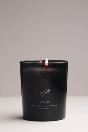 Illuminated YAFO SUEDE candle in a dark container on a white surface with a light gray background.