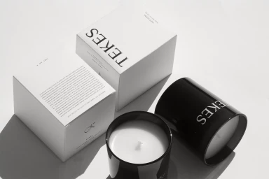 TEKES candle boxes and black glass candle jars arranged on a clean white surface with sharp shadows