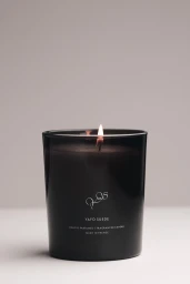 Black glass scented candle with a lit wick on a neutral grey background for TEKES brand identity.