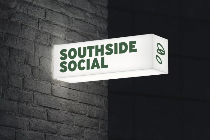 Illuminated sign for Southside Social mounted on a brick wall, photographed at night. The sign is white with green lettering.