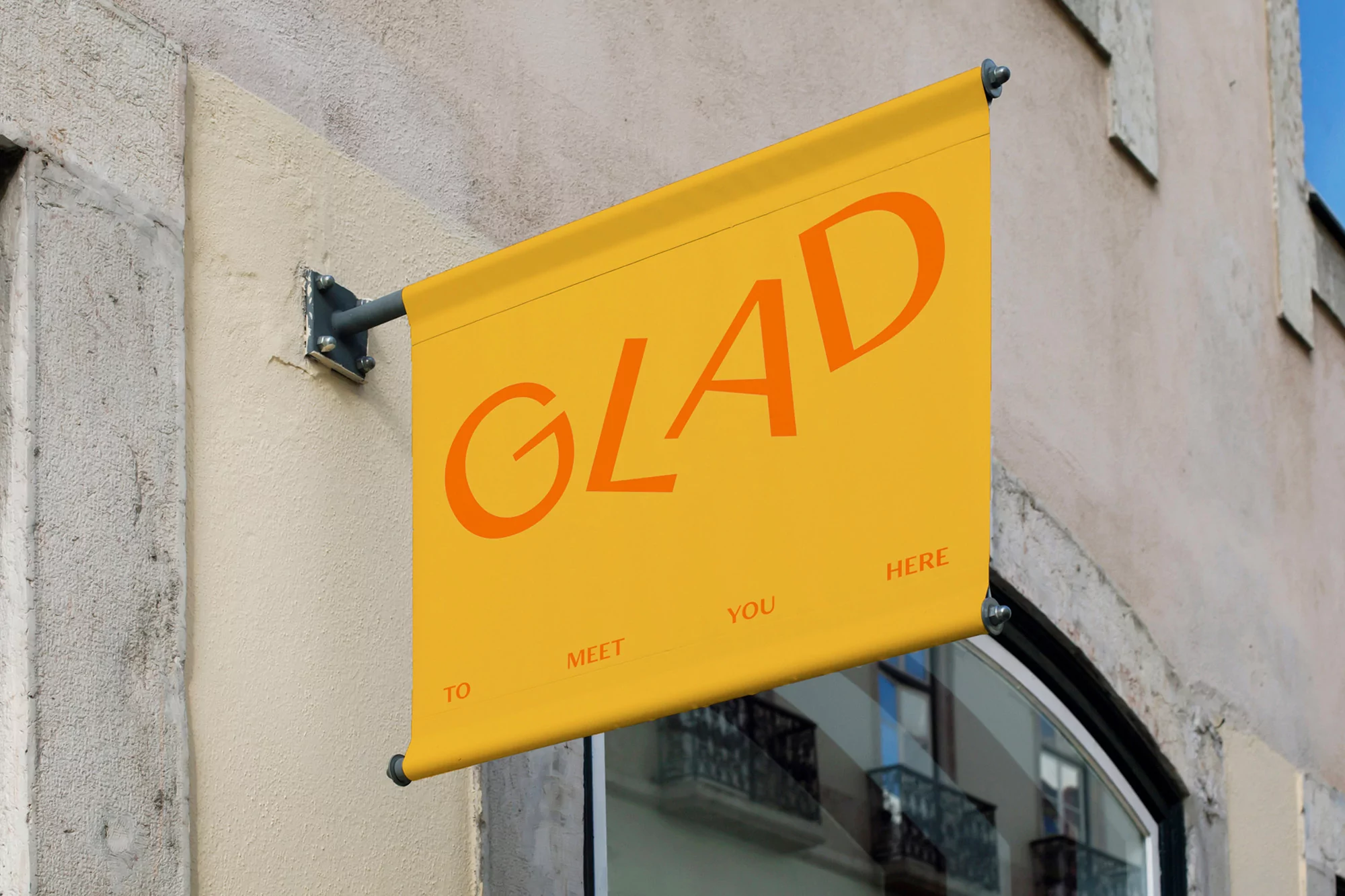 Eye-level shot of an orange-toned banner on a stone building with the text 'GLAD TO MEET YOU HERE' visible. The banner is mounted with gray metal hardware.