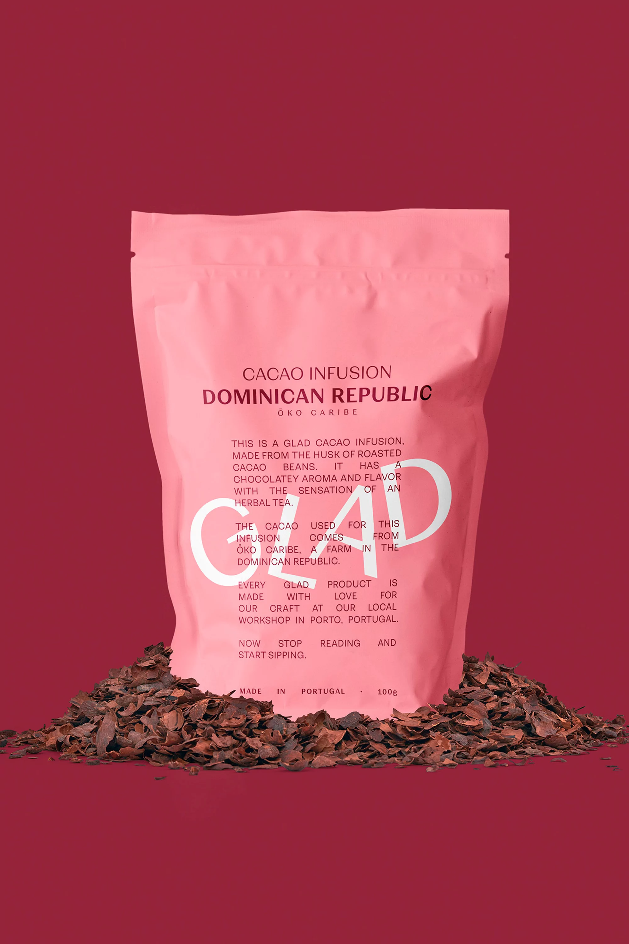 Pink package of cacao infusion from the Dominican Republic on pile of roasted cacao beans, studio shot on red background.
