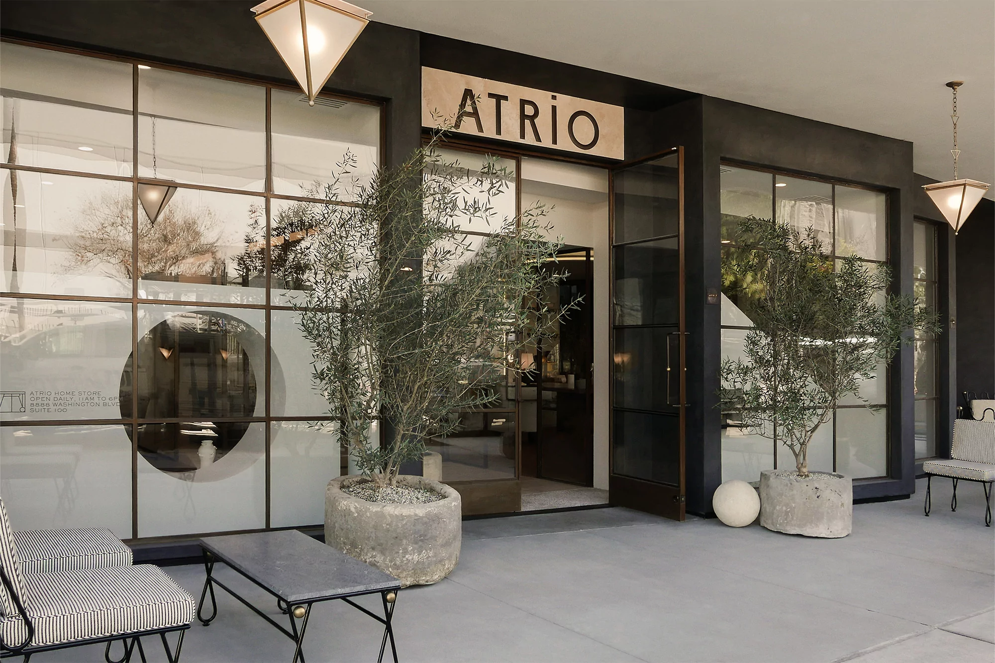 Exterior of Atrio Home Store with planters, furniture, and large windows in a modern architectural setting, bathed in soft light.