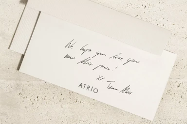 Handwritten note on a white card with an envelope resting on a textured stone surface for Atrio brand identity