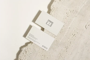 Two off-white minimalist business cards placed on a textured concrete surface under soft directional light