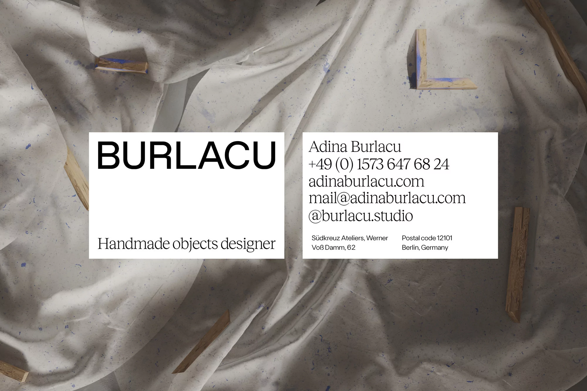 Artistic business card featuring brand name and contact details on a textured white fabric background with wooden pieces, clean aesthetic.