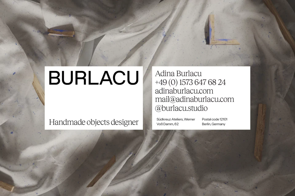 Artistic business card featuring brand name and contact details on a textured white fabric background with wooden pieces, clean aesthetic.