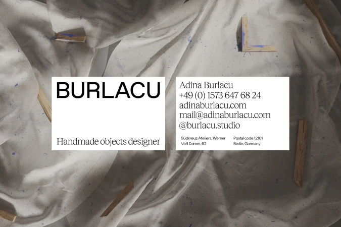 Artistic business card featuring brand name and contact details on a textured white fabric background with wooden pieces, clean aesthetic.
