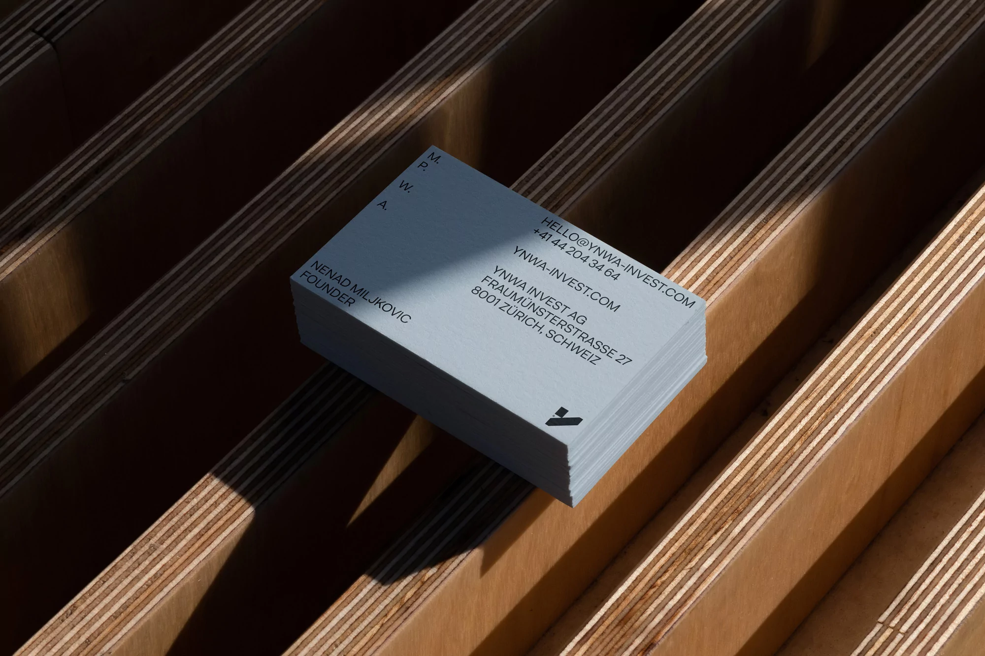 Stack of light blue business cards on a wood surface with the company name and contact information printed in a dark, sans-serif font.