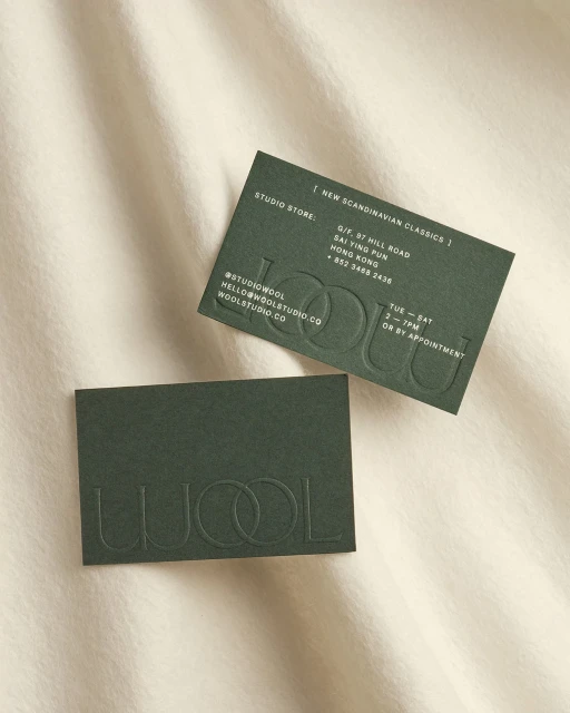 Two green business cards with embossed text on a cream-colored textured background. Modern business card design concept.